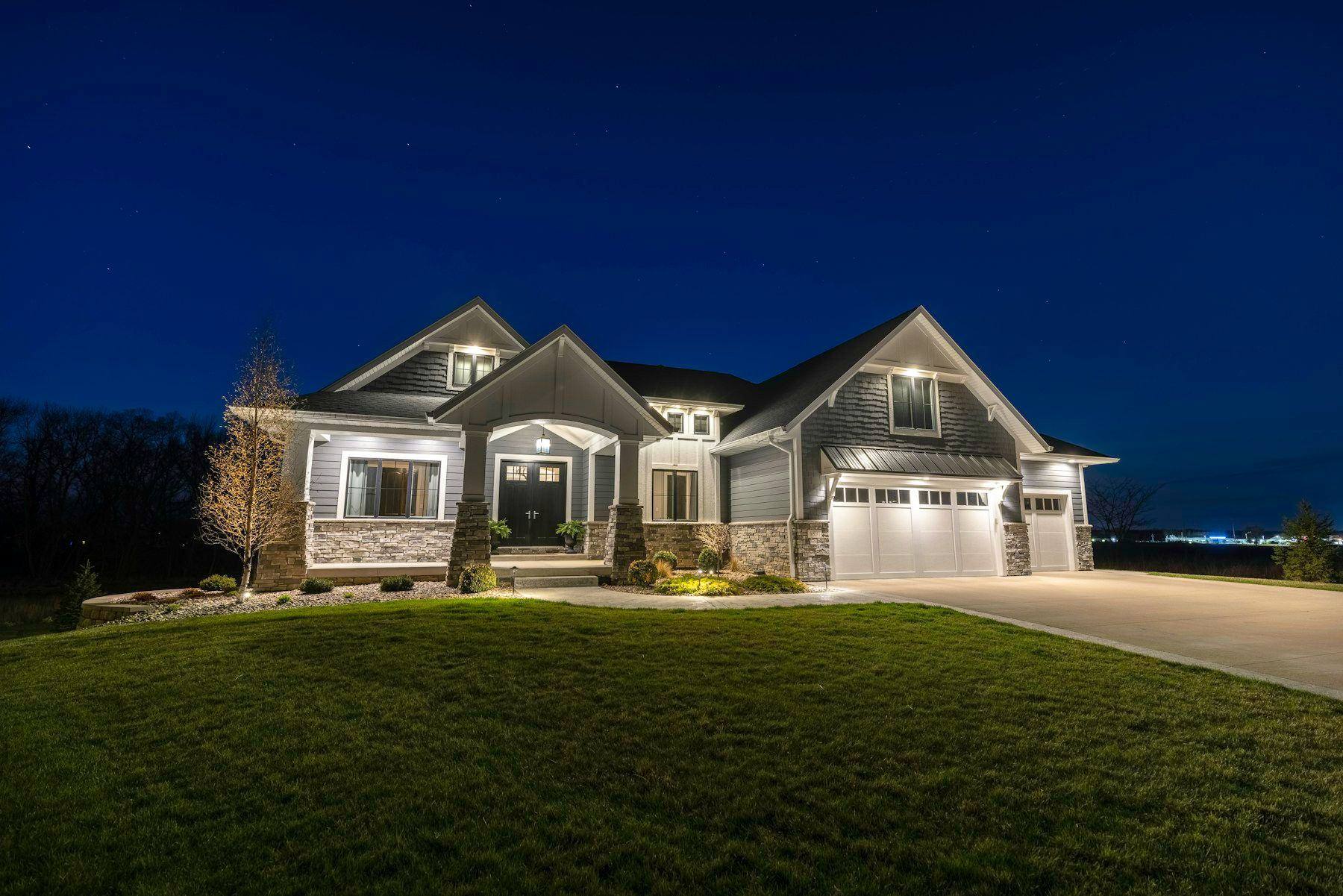 A two-story home with warm lights on at dusk